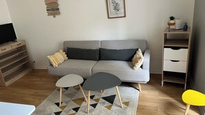 A modern living room with a grey sofa, two small tables, a patterned rug, a wooden TV stand, and a white cabinet. - Apartment historic center Monségur (Monségur)