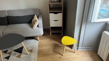 Een moderne woonkamer met een grijze bank, een kleine ronde tafel, een gele stoel en een radiator.