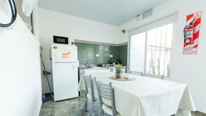 Een moderne keuken met een witte koelkast, magnetron en fornuis. Er is een eettafel met stoelen, een potplant en een raam met uitzicht.