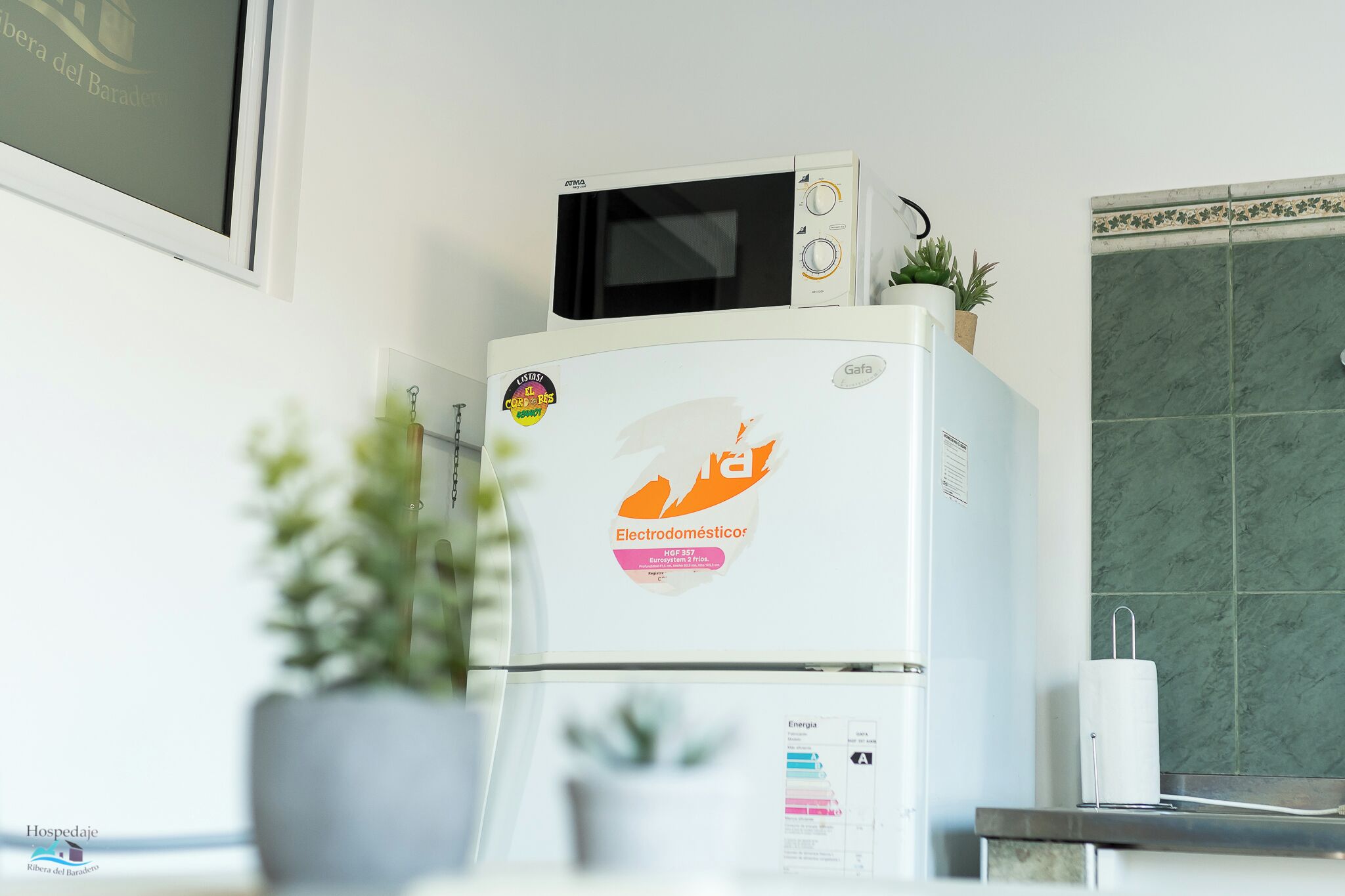 A kitchen with a white refrigerator, a microwave on top, and a tiled backsplash.