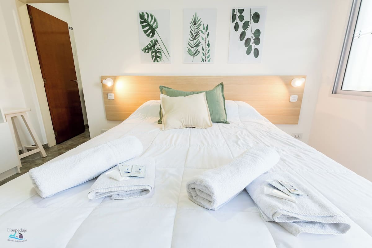 A hotel room with a bed, white towels, and green pillows. There are wall art pieces above the bed.