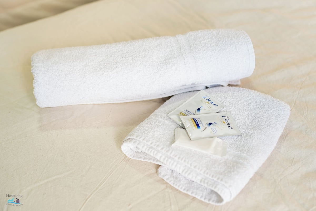 A neatly folded white towel and two Dove body lotion packets on a bed.