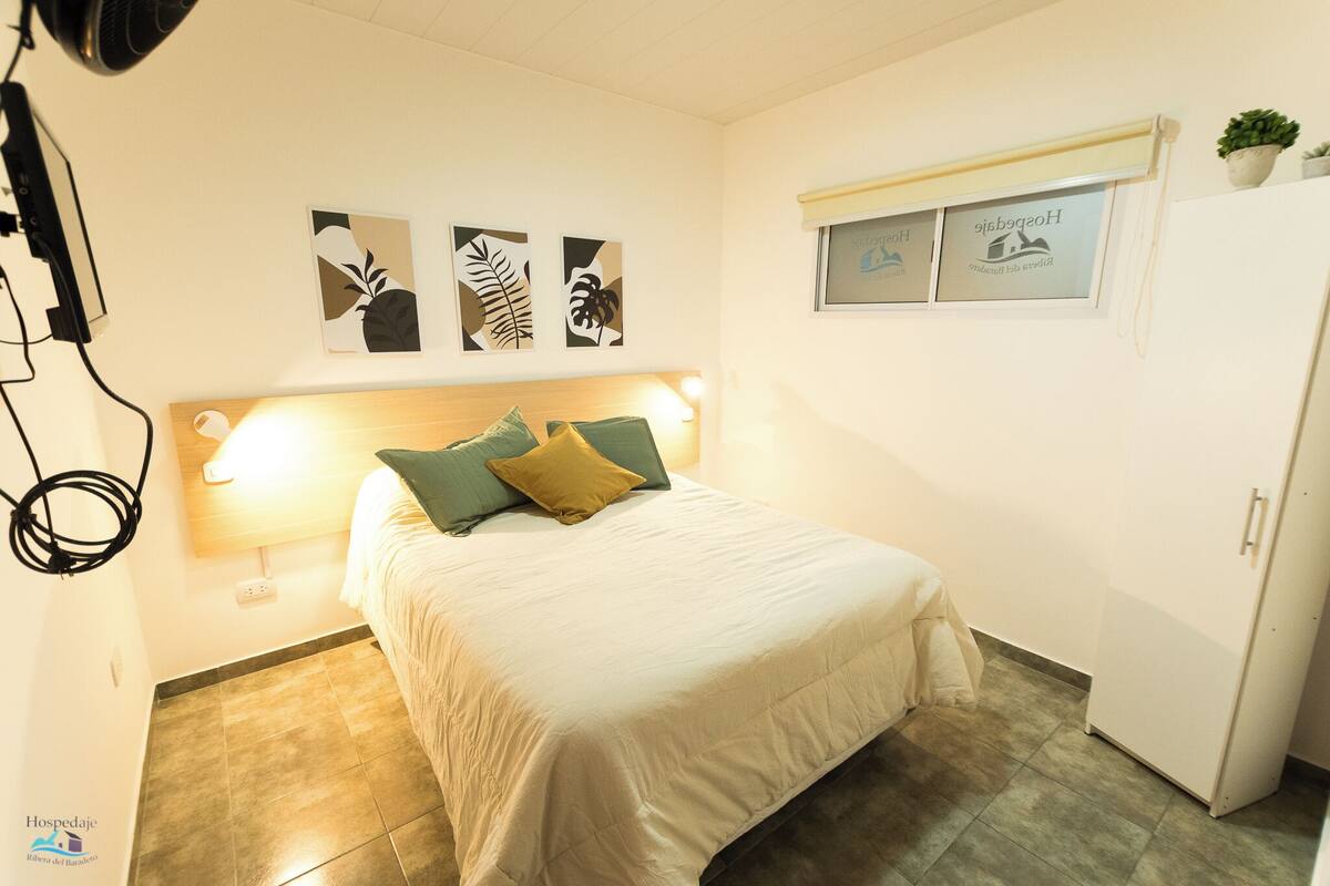 A hotel room with a bed, a bedside lamp, a wall-mounted TV, and a refrigerator.