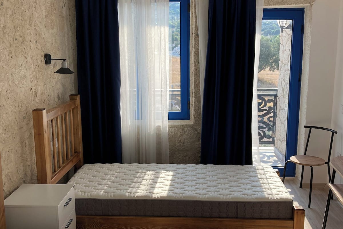 Une chambre à coucher avec un lit, un bureau, une chaise et une fenêtre avec des rideaux.