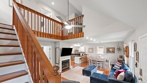 A spacious living area with a wooden staircase, a fireplace, a television, and a dining area with a table and chairs.