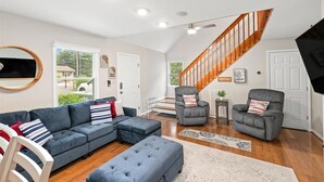 A spacious living room with a large sectional sofa, two armchairs, a wooden staircase, and a view of the outside.
