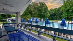 A covered outdoor area with a pool, picnic tables, and umbrellas.