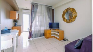 A modern living room with a flat-screen TV on a wooden stand, a purple sofa, and a large mirror on the wall. - Comfortable And Tidy Studio At Titanium Square Apartment (Jakarta)