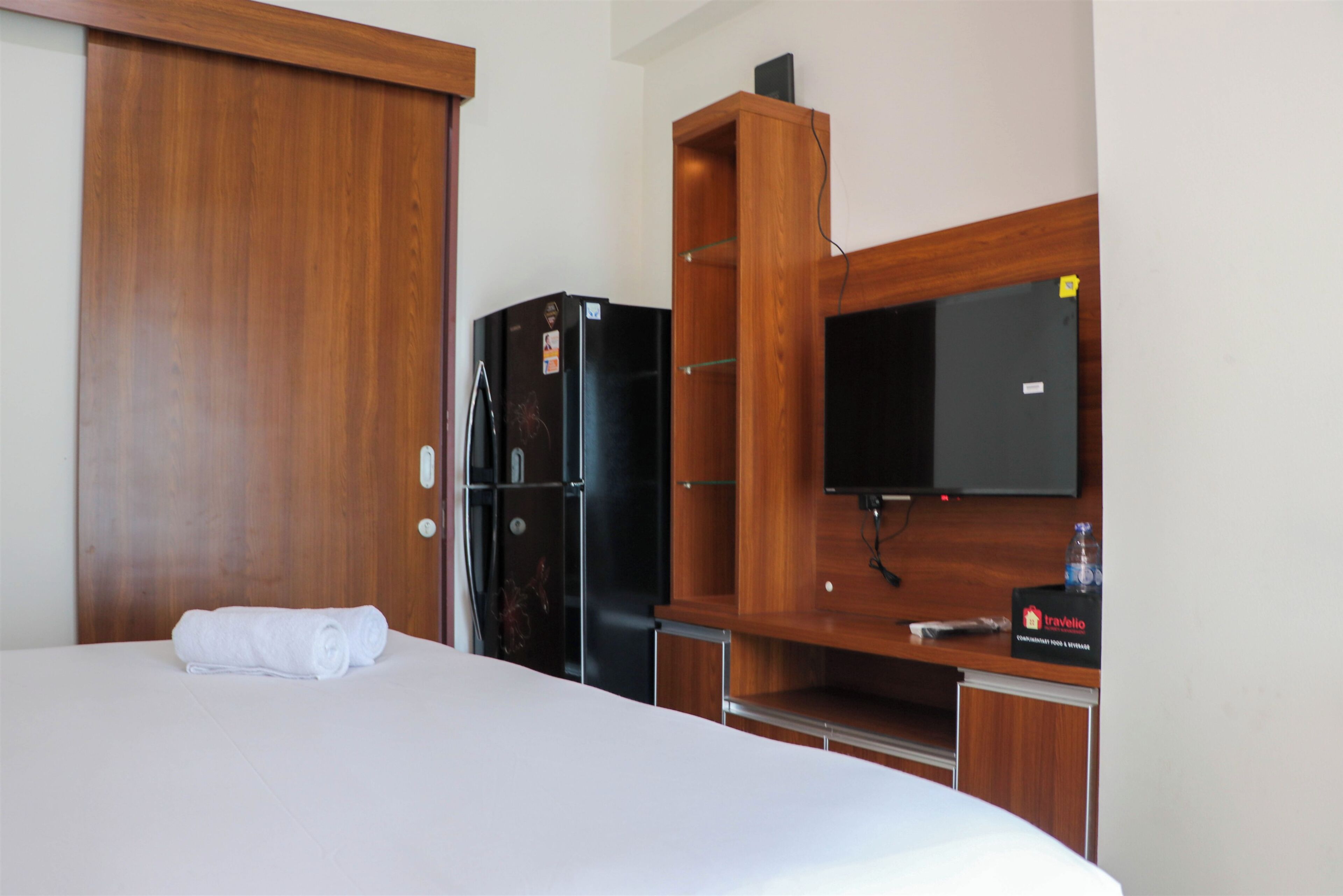 Una habitación de hotel con una cama, un armario de madera, un refrigerador negro y un televisor montado en la pared.