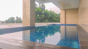 Une piscine à l’eau d’un bleu limpide, entourée de murs recouverts de carreaux et de piliers en béton.
