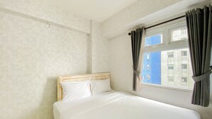 Une chambre à coucher avec un lit, une fenêtre avec des rideaux et une vue sur les bâtiments à l’extérieur.