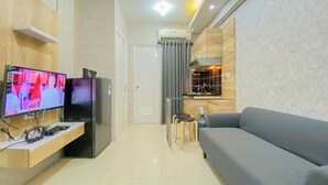 Un salon moderne doté d’un téléviseur à écran plat, d’un réfrigérateur noir, d’un canapé gris et d’un petit coin cuisine avec une cuisinière et des chaises.
