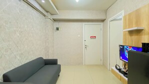 Une pièce comprenant un canapé, un téléviseur posé sur un meuble, une porte avec une pancarte rouge et un luminaire au plafond.