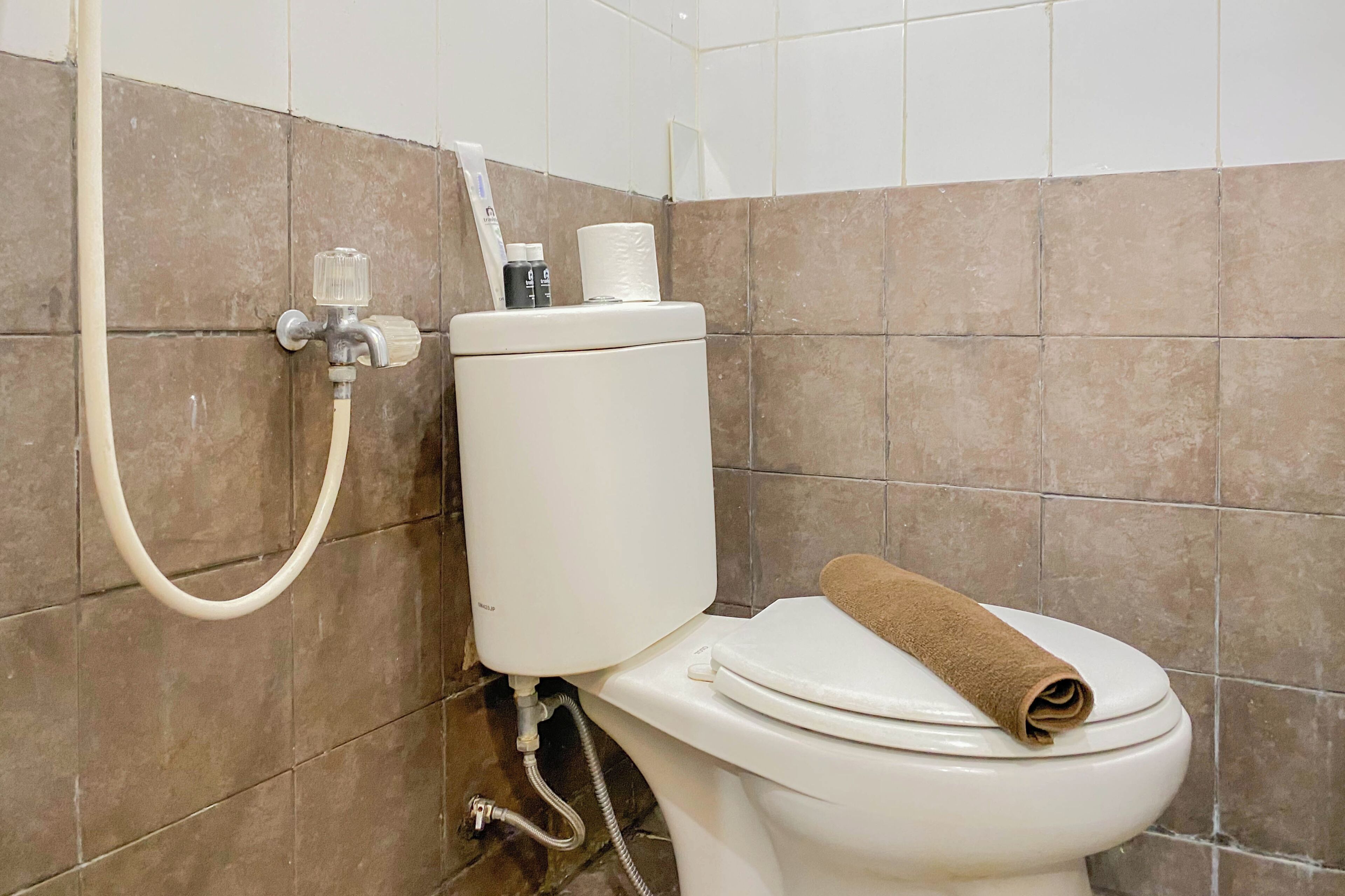Casa de banho com sanita, chuveiro e suporte de papel higiénico fixado na parede.