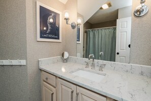 A bathroom with a marble sink, a mirror, and a framed poster of a lighthouse. - Renovated Dog-Friendly Waterfront Condo (Manistee)