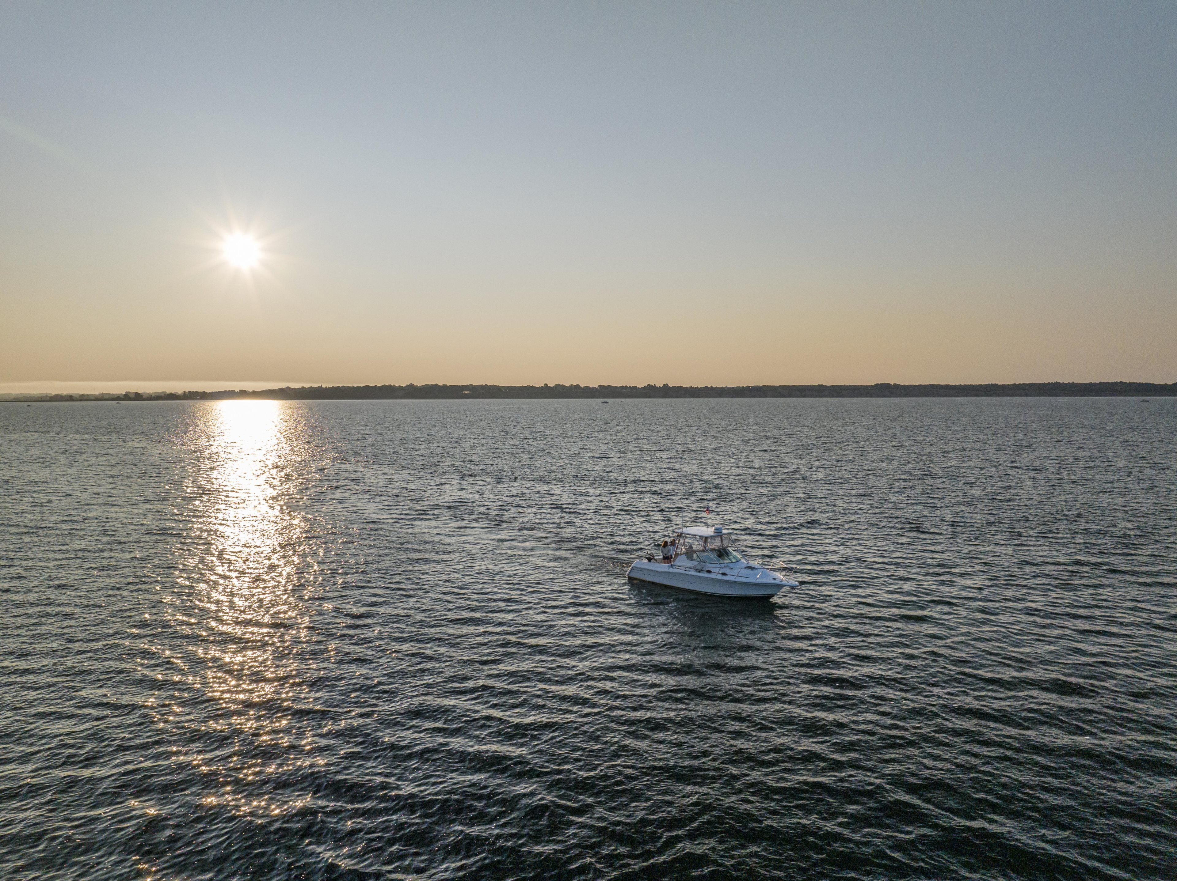 A boat on calm water with a clear sky and the sun low on the horizon.