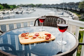 A table with a glass of red wine, a glass of white wine, and a wooden board with sliced meats and cheese on a balcony overlooking a marina. - Renovated Dog-Friendly Waterfront Condo (Manistee)