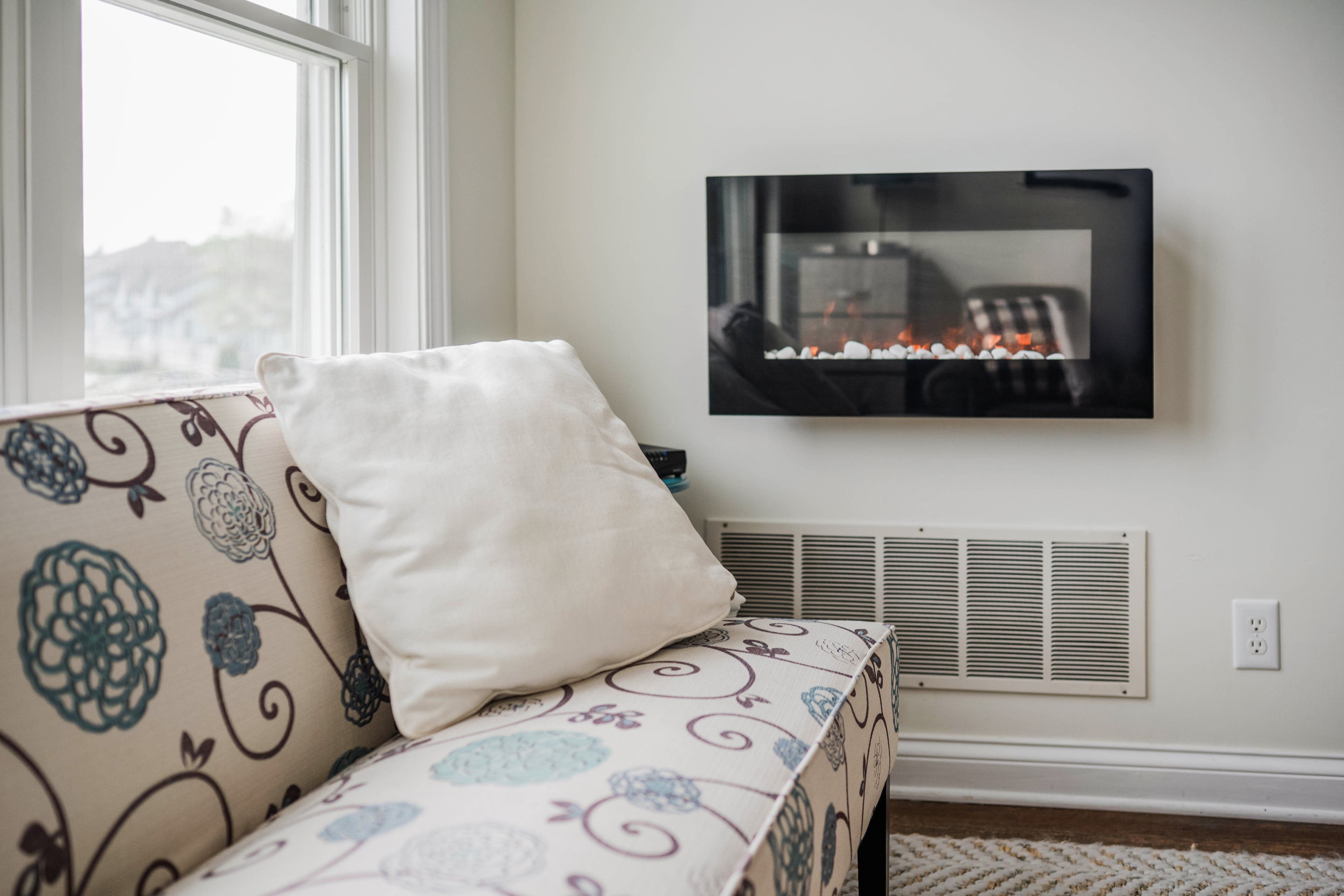 Een woonkamer met een bank, een tv aan de muur en een ventilatierooster.