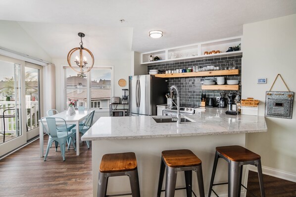 A modern kitchen with a large island, bar stools, and a dining area with blue chairs.