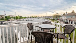 En balkon med fletstole og et bord med udsigt over en lysthavn med både og huse i baggrunden.