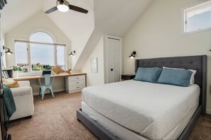 A bedroom with a large bed, a desk with a chair, a window, and a ceiling fan. - Renovated Dog-Friendly Waterfront Condo (Manistee)