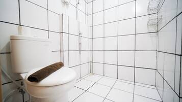 Baño con azulejos blancos, inodoro y zona de ducha.
