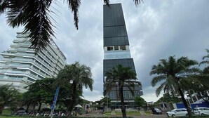 A tall, modern skyscraper with a glass facade, surrounded by palm trees and other greenery. - Good And Restful 1Br At The Smith Alam Sutera Apartment (Tangerang)