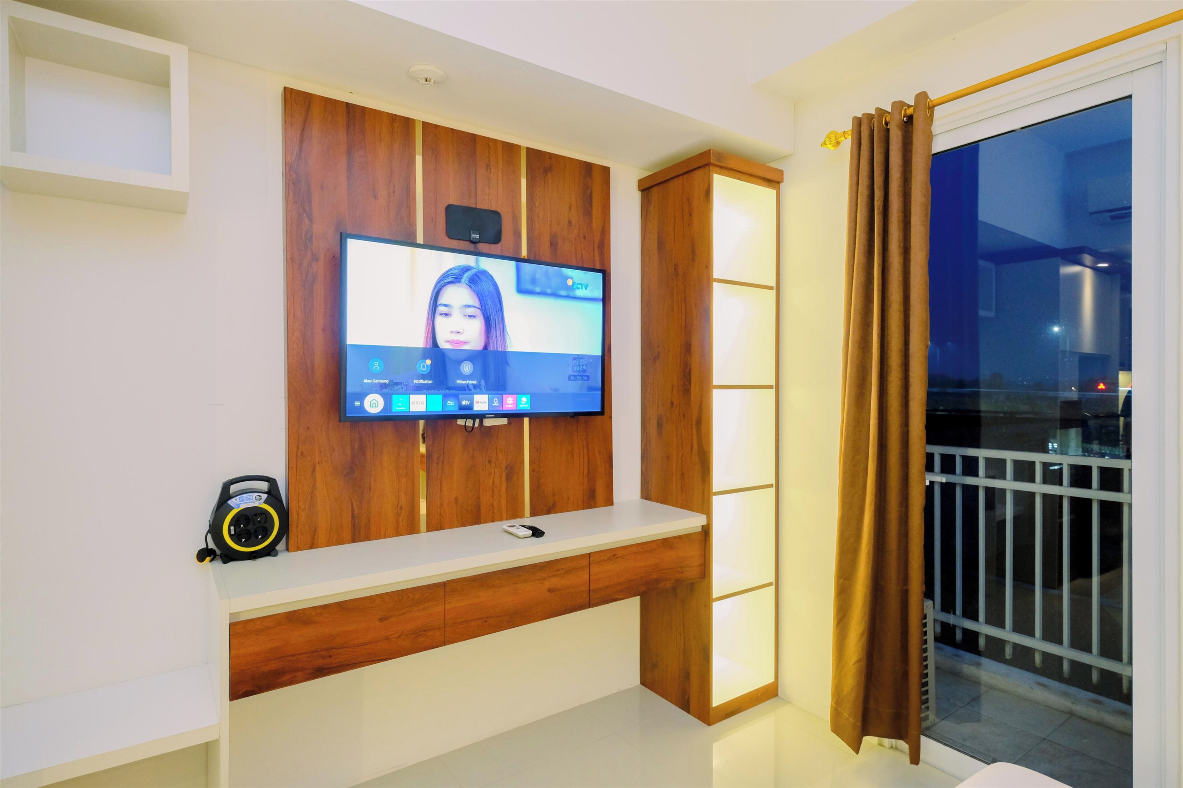 Ein modernes Wohnzimmer mit einem an der Wand befestigten Fernseher, Holzvertäfelung, einem weißen Konsolentisch und einem Balkon mit Blick.