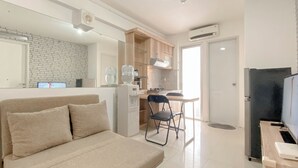 A modern, well-lit room with a sofa, a dining table with chairs, a kitchen area, and a refrigerator.