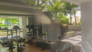 A gym with various exercise equipment, including treadmills and elliptical machines, and a view of palm trees and greenery outside.