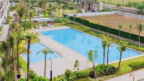 A large swimming pool surrounded by palm trees and greenery, with a view of a residential area in the background. - Good Designed And Restful Studio Sky House Bsd Apartment (Pagedangan)