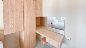 A compact bedroom with a wooden wardrobe, a small desk, and a single stool.