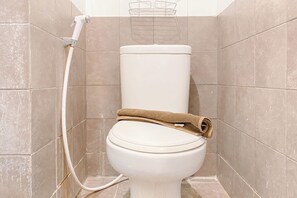 Un inodoro con una toalla encima, una manguera de ducha y azulejos color beige.