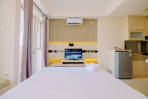 Een hotelkamer met een bed, een televisie op een standaard, een minibar en een kitchenette.