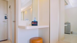 Een hotelbadkamer met een spiegel, een plank met toiletartikelen en een houten kruk.