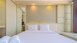 Een hotelkamer met een groot bed, twee kussens, een nachtkastje en een opgerolde witte handdoek.