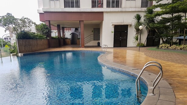 Una piscina con bordo piastrellato, un corrimano in metallo e un edificio con un balcone sullo sfondo.