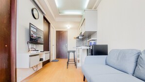 Un ambiente compatto con angolo cottura, divano, televisore e una sveglia appesa al muro.