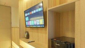 A room with a mounted television displaying various apps, a remote control, and a Philips printer on a wooden shelf. - Cozy Living 2Br At Tokyo Riverside Pik 2 Apartment (Teluknaga)