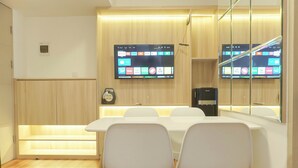 A modern conference room with a long table, white chairs, a flat-screen TV mounted on the wall, and a wooden panel design. - Cozy Living 2Br At Tokyo Riverside Pik 2 Apartment (Teluknaga)
