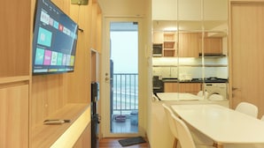 A compact hotel room with a wooden interior, a TV mounted on the wall, a balcony with a view, and a kitchenette. - Cozy Living 2Br At Tokyo Riverside Pik 2 Apartment (Teluknaga)