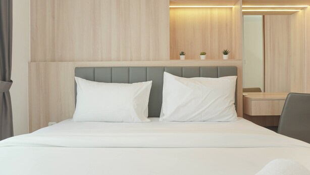 A hotel room with a bed, a bedside table, a mirror, and a small potted plant. - Cozy Living 2Br At Tokyo Riverside Pik 2 Apartment (Teluknaga)
