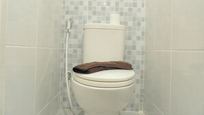Des toilettes avec une serviette marron posée sur la cuvette, un porte-rouleau de papier toilette et un tuyau de douche.