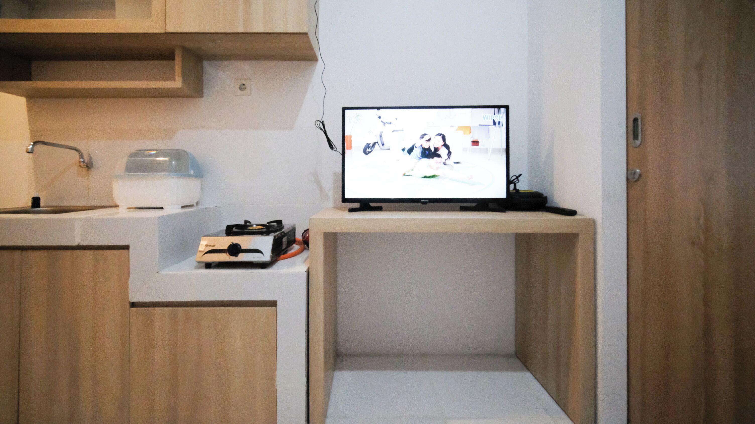 Una pequeña kitchenette con estufa, hervidor y televisor de pantalla plana sobre un mueble.