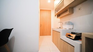 A narrow kitchen with white cabinets, a wooden door, and a countertop with a kettle and a box. - Simple And Comfortable Living 1Br At The City Square Apartment (Surabaya)