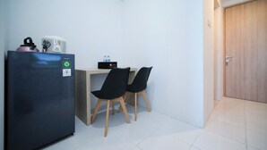 A compact room with a refrigerator, a small table, two chairs, and a wooden door. - Simple And Comfortable Living 1Br At The City Square Apartment (Surabaya)