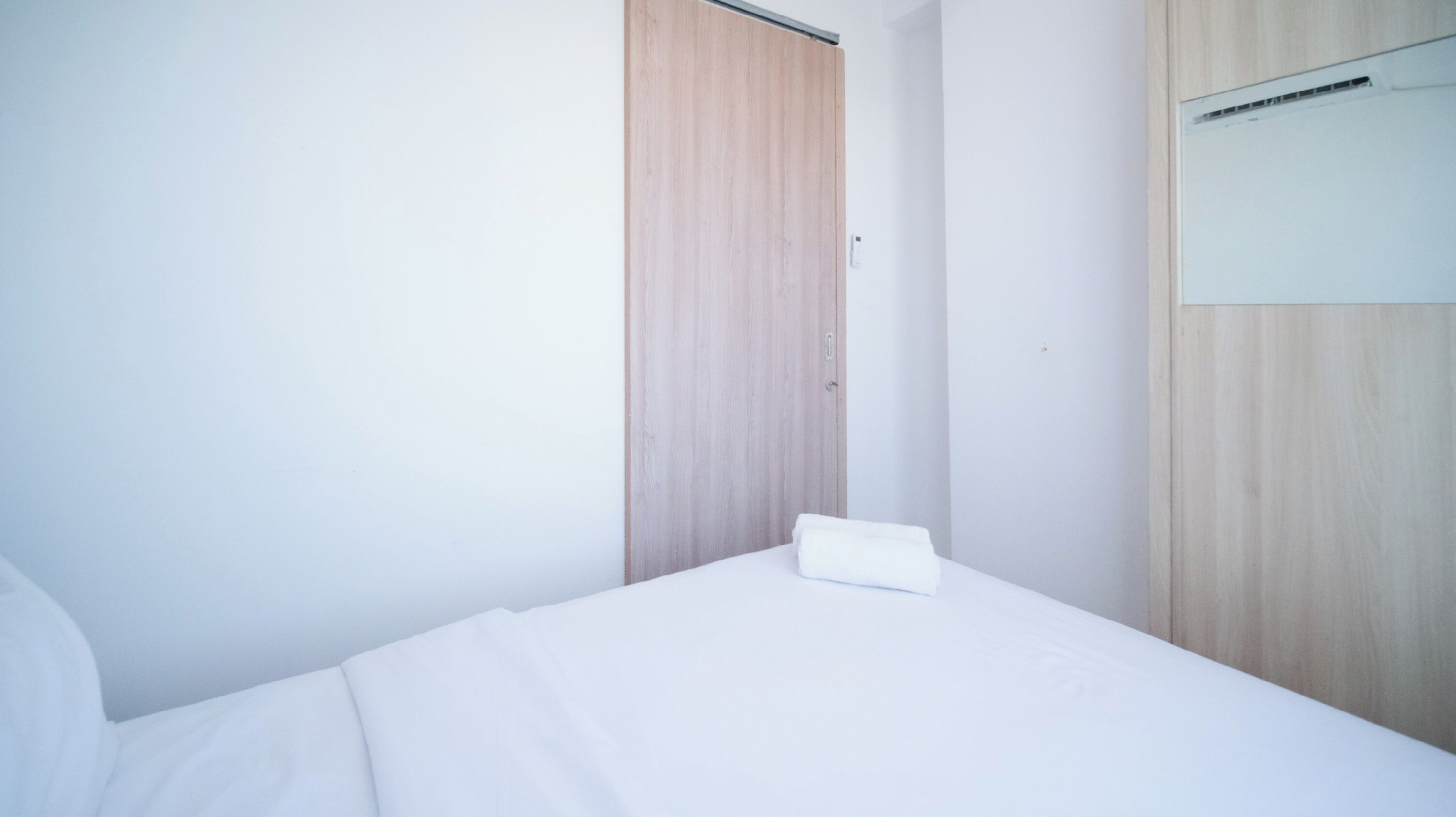 A neatly made bed with white bedding in a room with light wooden walls and a wooden door.