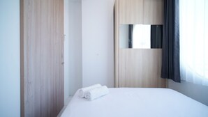 A hotel room with a wooden wardrobe, a bed with white linens, and a mirror on the wall. - Simple And Comfortable Living 1Br At The City Square Apartment (Surabaya)