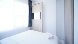 A hotel room with a bed, a wooden wardrobe, and a window with curtains. - Strategic And Homey 1Br At The City Square Apartment (Surabaya)
