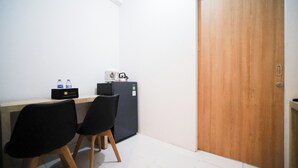 A small room with a desk, two chairs, a refrigerator, and a wooden door. - Strategic And Homey 1Br At The City Square Apartment (Surabaya)